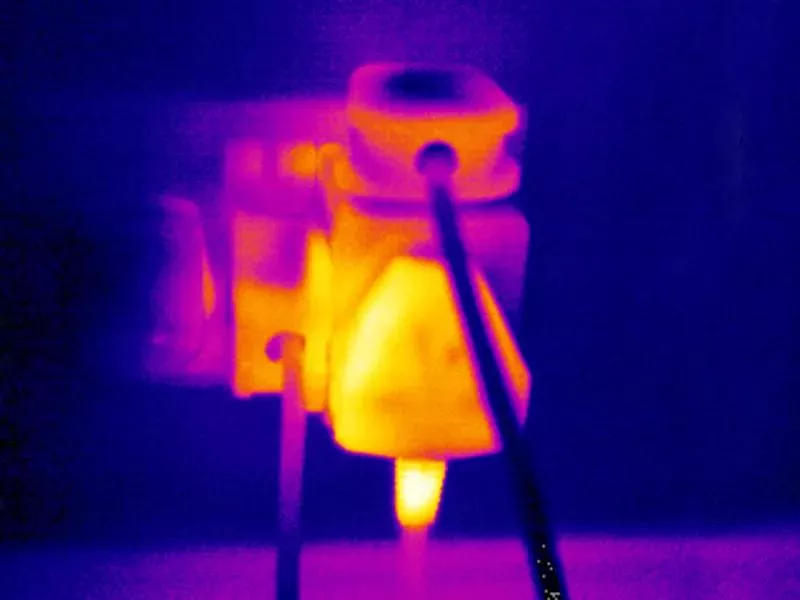 The distinctive black, gray, and white tones of infrared imaging interweave to outline the bustling production scene of the industrial pipeline. Heat sources, a blend of dark red and bright white, dance across the frame. Mechanical arms precisely grasp high-temperature metal components. The bright white high-temperature areas at their joints starkly contrast with the surrounding dark gray cool tones, as if narrating the continuous operation under high-intensity workloads. The conveyor belt, like a winding dark river, carries semi-finished products that glow with a grayish-white sheen, moving forward at a steady pace. In the distance, the control console emits a soft orange light, and the figures of the workers appear as blurred gray shadows, attentively monitoring every production process in this technologically charged infrared world. The entire scene is imbued with both the powerful sense of industry and the ordered beauty of precise operation.